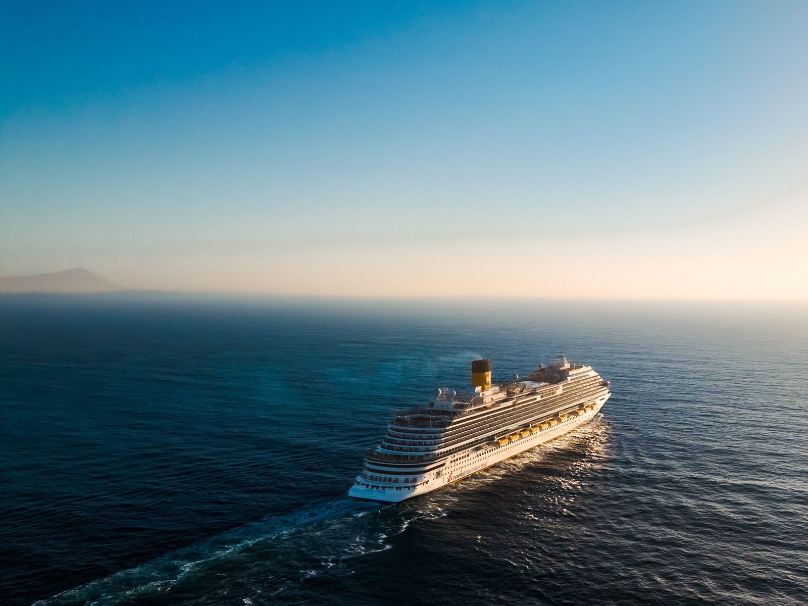 Aerial view of a cruise ship crossing calm ocean at sunset, the open-sea days of repositioning cruises in 2027