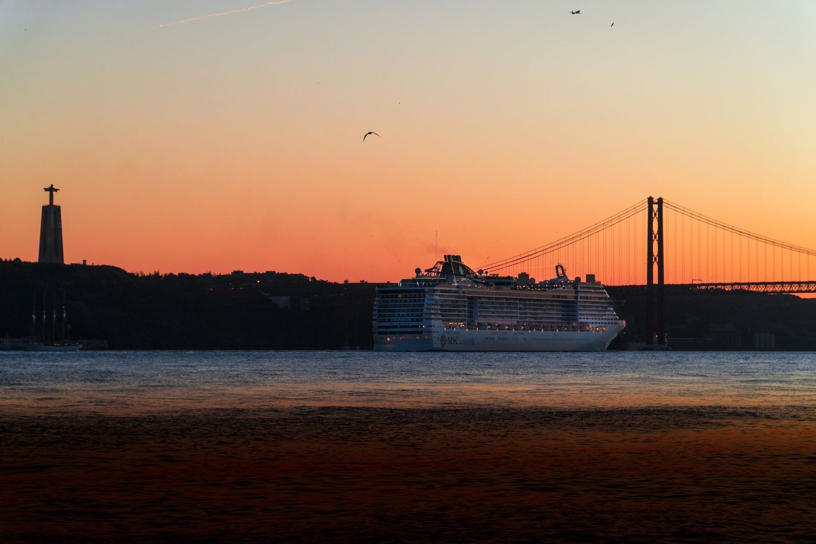 Cruise ship passing under the 25 de Abril Bridge in Lisbon at sunset