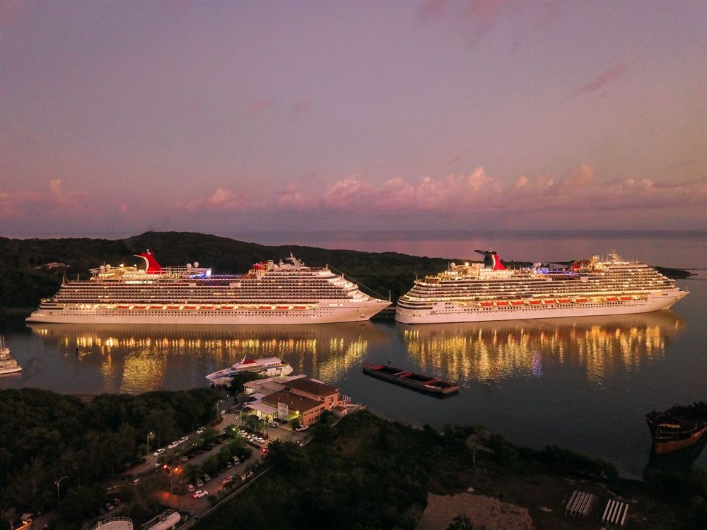 Two illuminated Carnival cruise ships docked at Coxen Hole, Honduras, at twilight